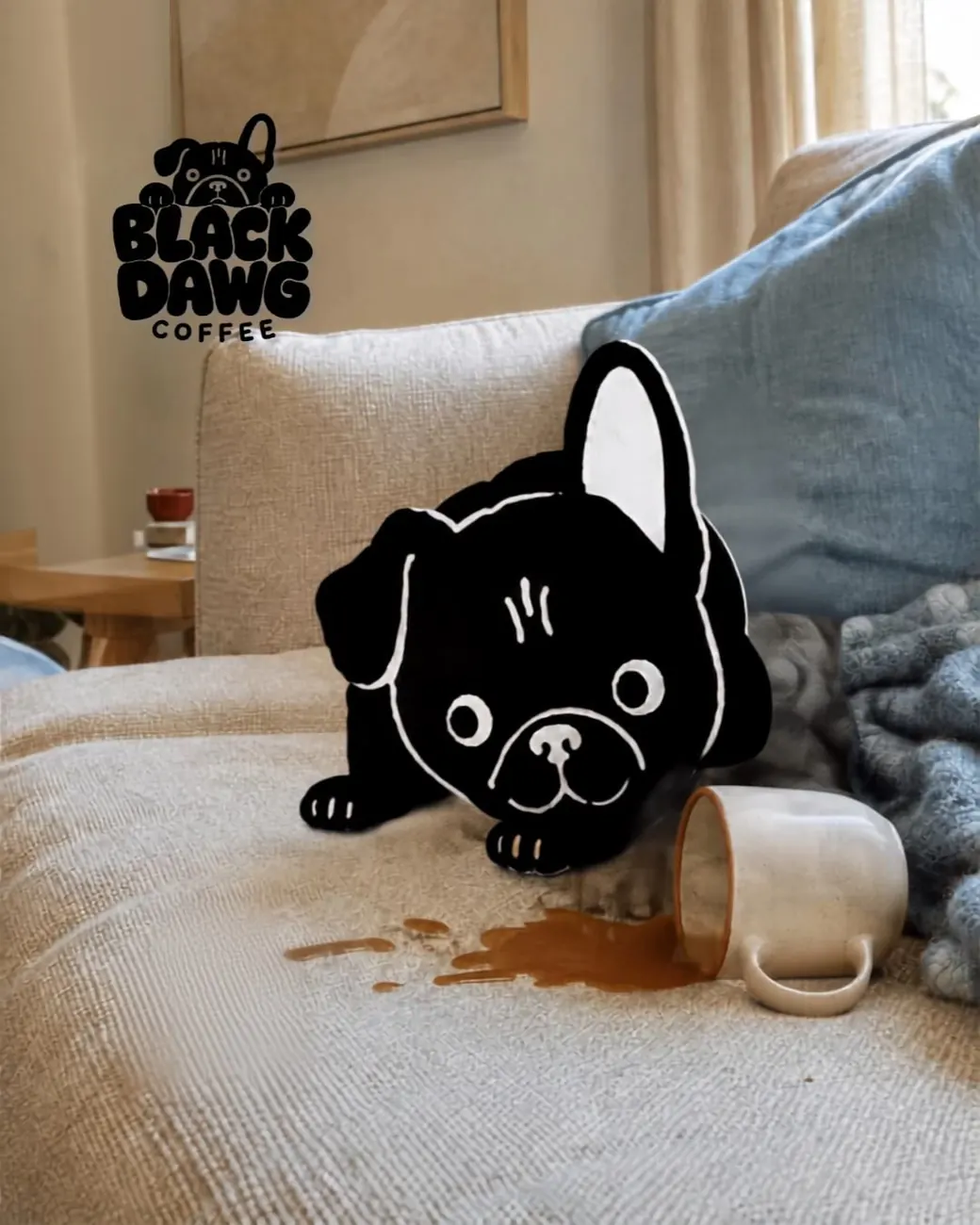 Black Dawg mascot on a sofa beside a knocked-over mug and a coffee spill