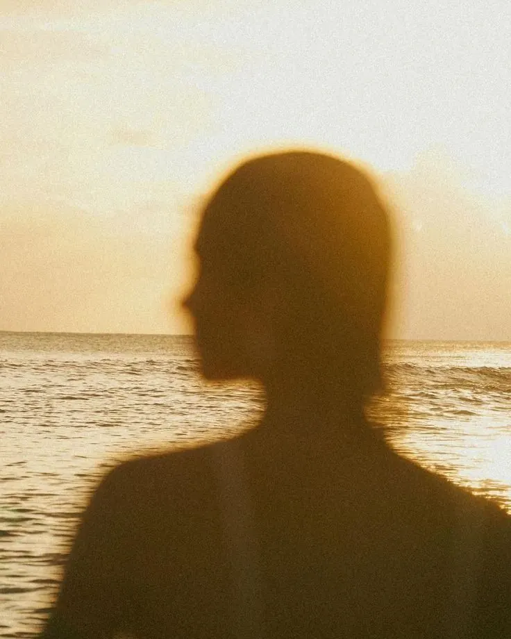 Silhouette of a woman against a low sun over water