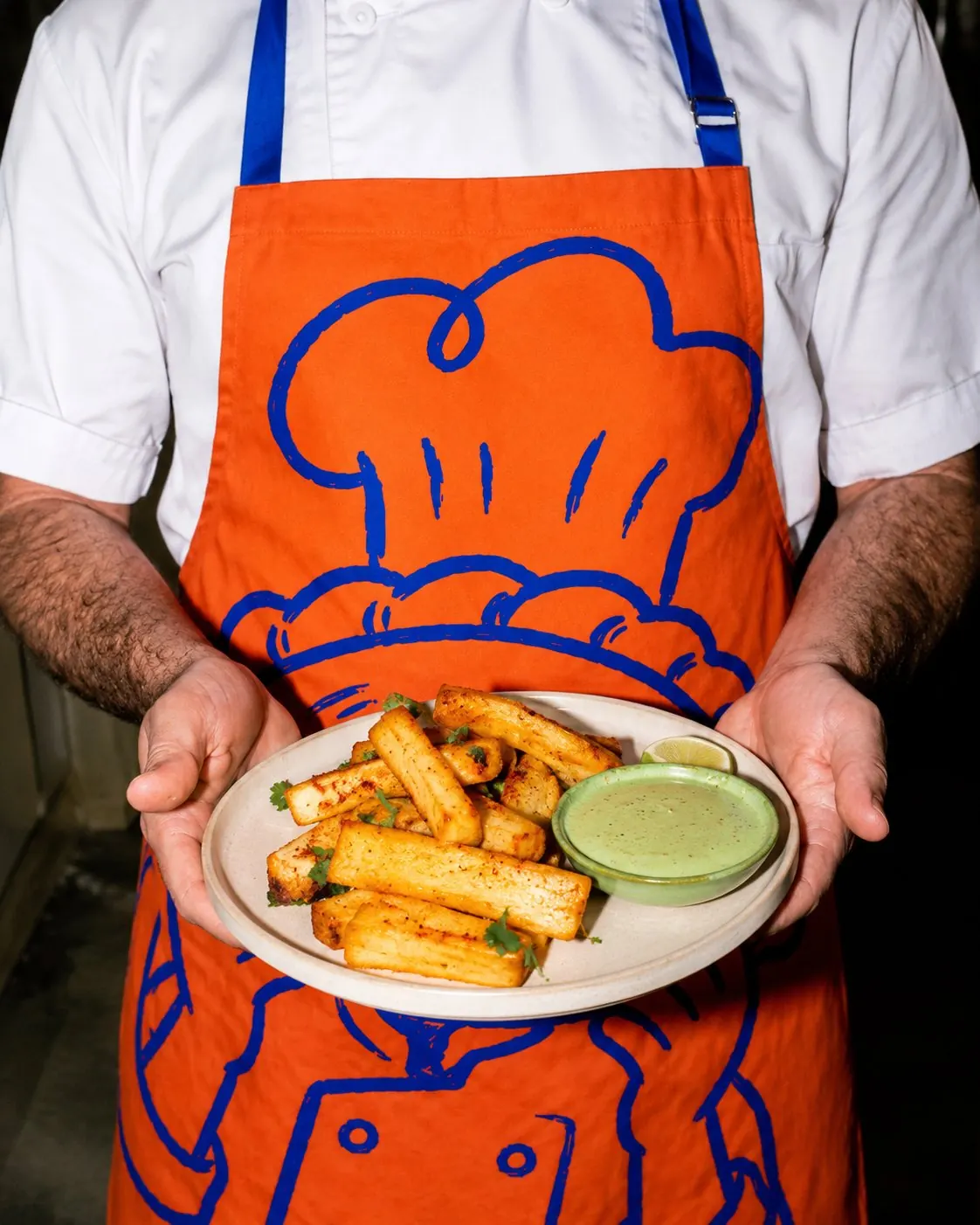 Chef in an orange Sin Cara apron holding a plate of fries, cropped at the chest