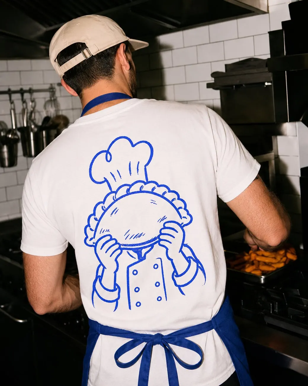 Cook seen from behind in the kitchen, wearing a white Sin Cara T-shirt